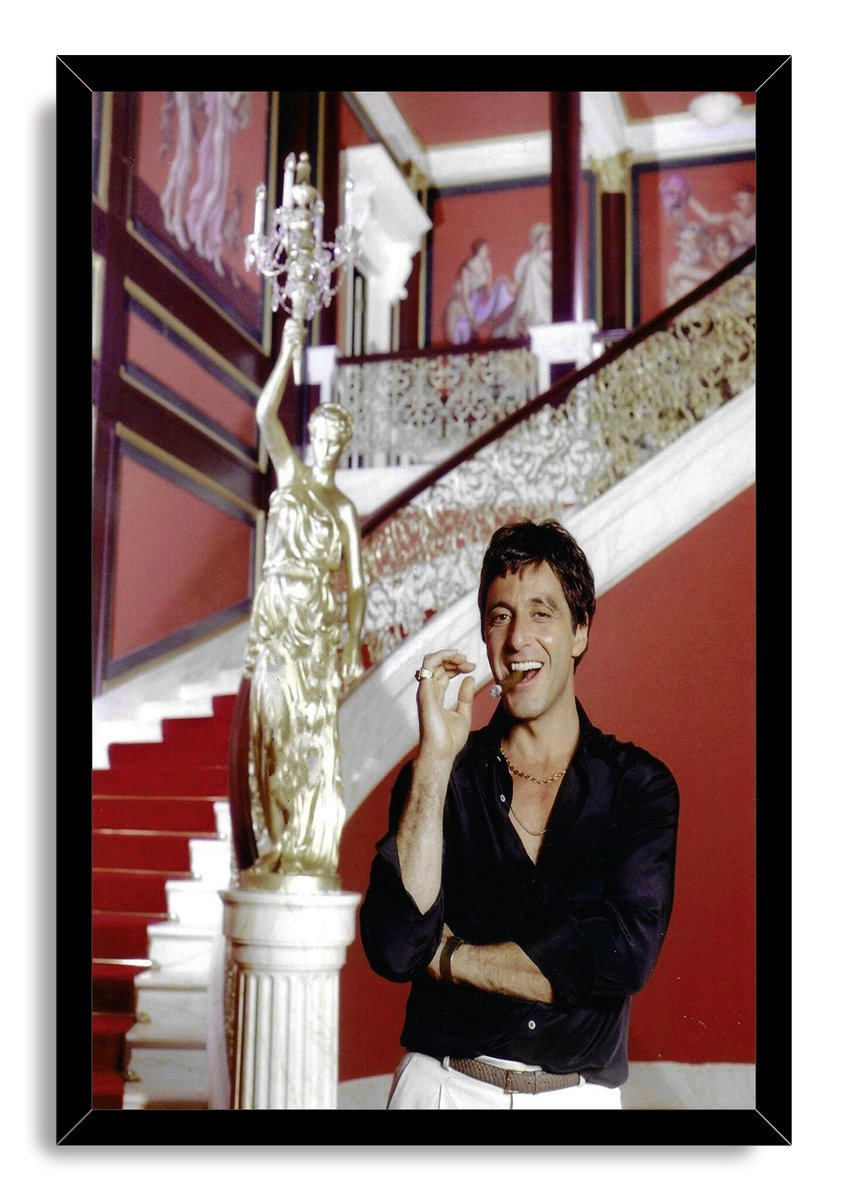 Tony Montana framed wall art print portrays Al Pacino smiling with a cigar in a lavish red interior with a staircase.