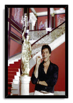 Tony Montana framed wall art print portrays Al Pacino smiling with a cigar in a lavish red interior with a staircase.