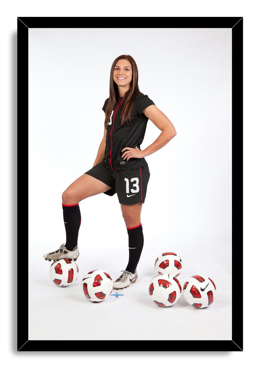 Alex Morgan framed wall art print portrays a smiling player in black soccer gear surrounded by five white and red soccer balls.