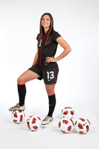 Alex Morgan wall art print features a smiling soccer player in a black number 13 kit posed among white and red balls.