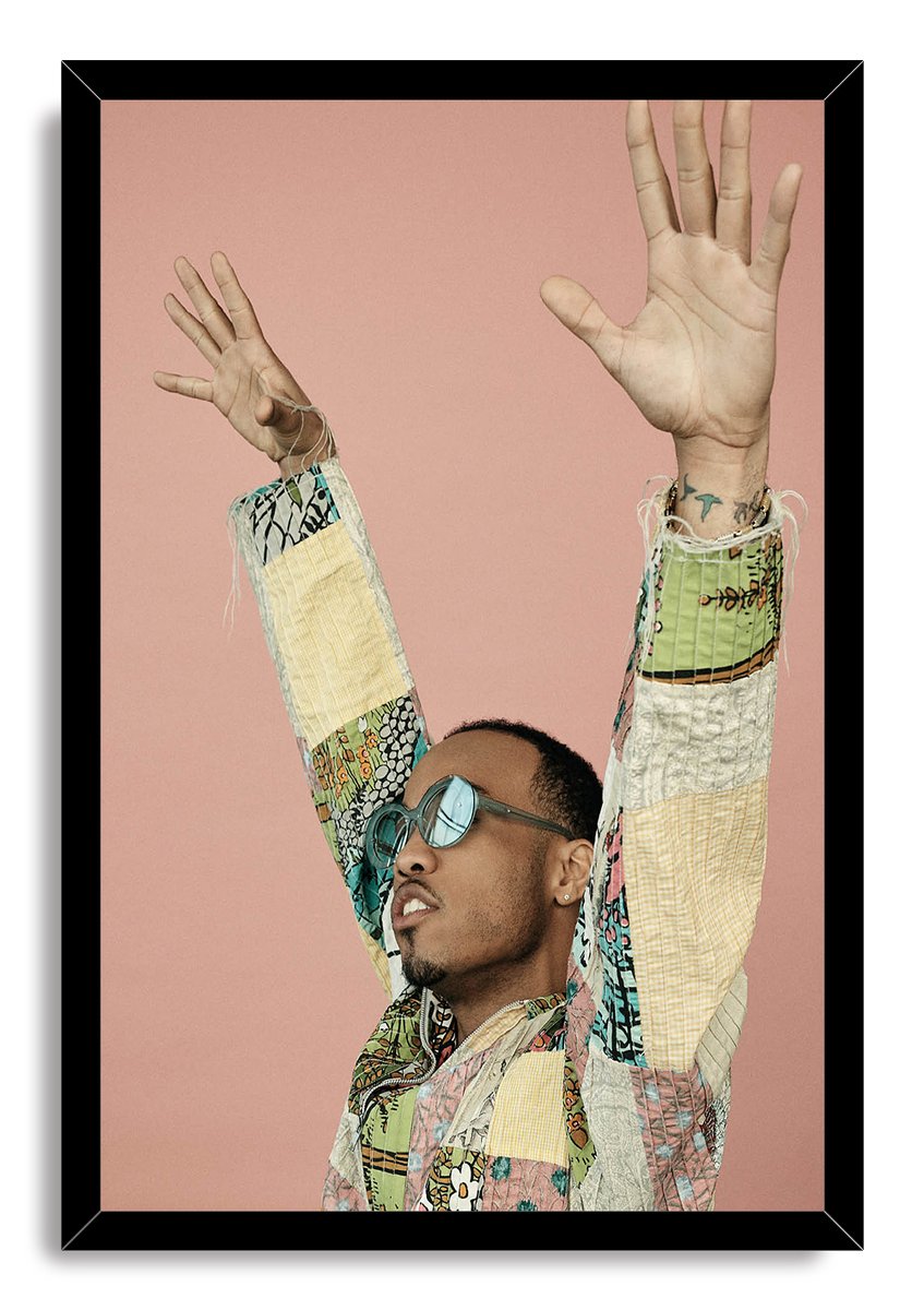 Anderson .Paak framed wall art print depicting the musician with uplifted arms in sunglasses and a patterned patchwork jacket.