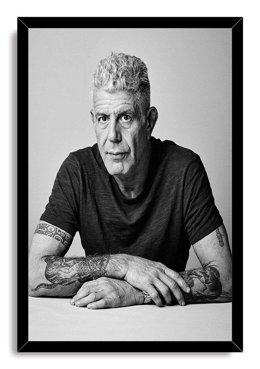 Anthony Bourdain framed wall art print displays a black-and-white seated portrait with tattooed forearms inside a black frame.