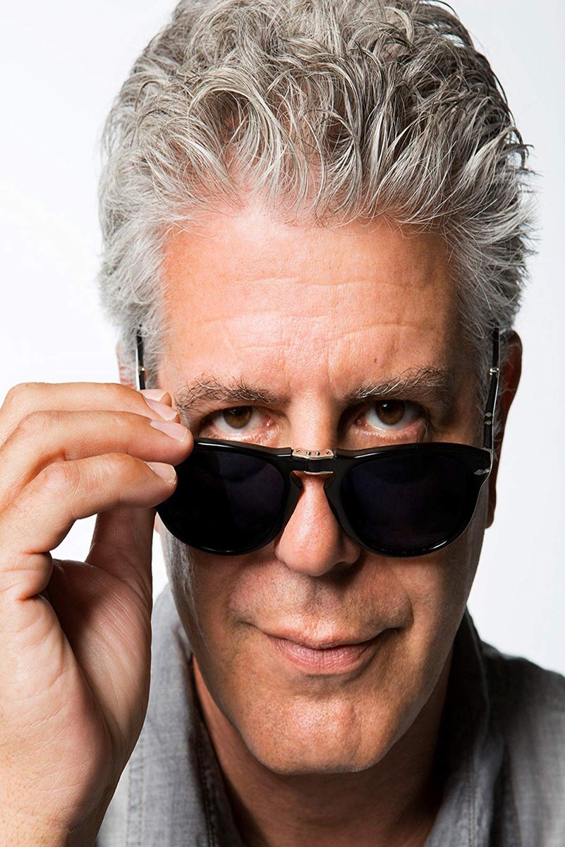 Anthony Bourdain poster portrait with silver hair, lifting black sunglasses to reveal his eyes against a white background.