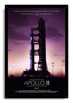 Apollo 11 framed wall art print presents a Saturn V on its launchpad against violet clouds, set in a black mitered frame.