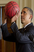 Barack Obama poster features him in a dark suit raising a red signed basketball indoors beside a microphone.