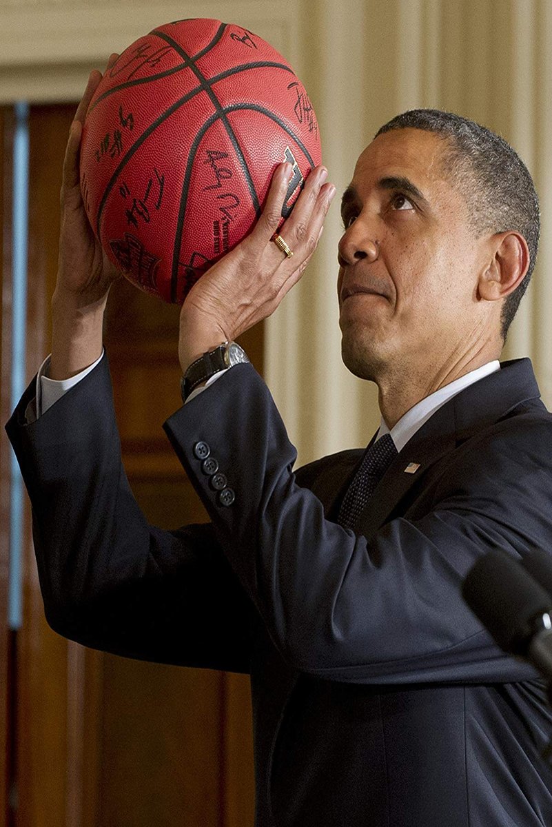 Barack Obama poster features him in a dark suit raising a red signed basketball indoors beside a microphone.