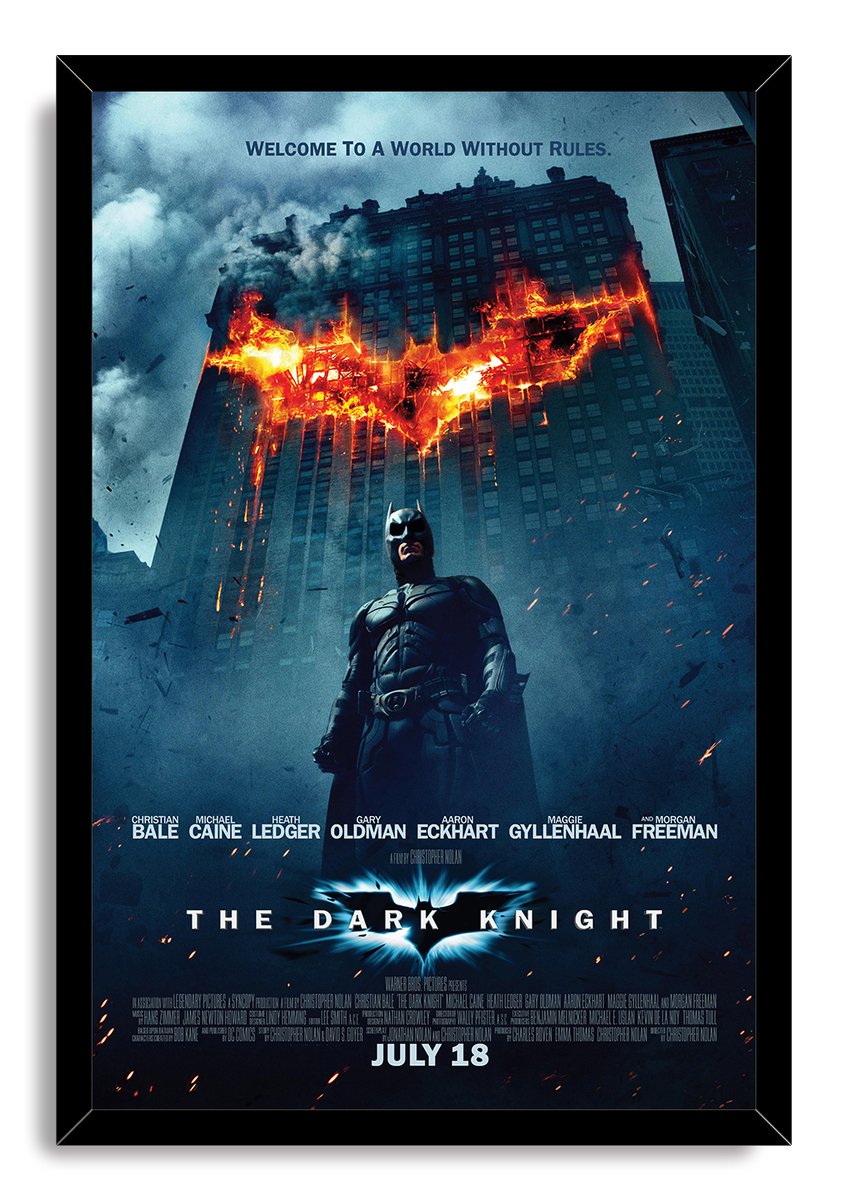 Batman The Dark Knight framed wall art print features Batman standing below a burning bat emblem against a stormy blue cityscape.