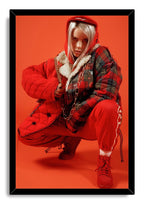 Billie Eilish framed wall art print depicts the singer crouched in a red hood and quilted plaid jacket, set within a black frame.