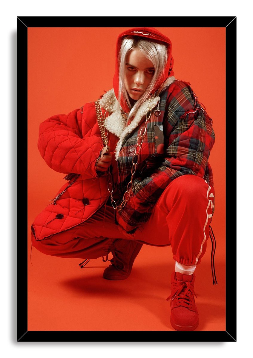 Billie Eilish framed wall art print depicts the singer crouched in a red hood and quilted plaid jacket, set within a black frame.