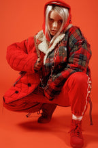 Billie Eilish poster features the singer crouching against a vivid red backdrop in layered red and plaid outerwear with gold chains.