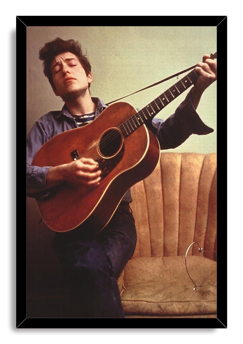 Bob Dylan framed wall art print portrays the musician strumming a brown acoustic guitar beside a tan chair in warm vintage tones.