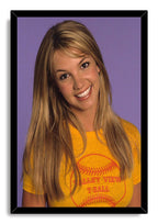 Britney Spears framed wall art print with a black border, portraying her smiling in a yellow T-shirt against purple.
