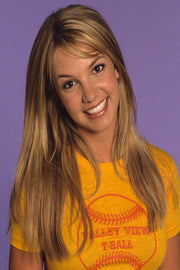 Britney Spears poster portrait with long blonde hair, smiling in a yellow T-shirt against a lavender-purple background.