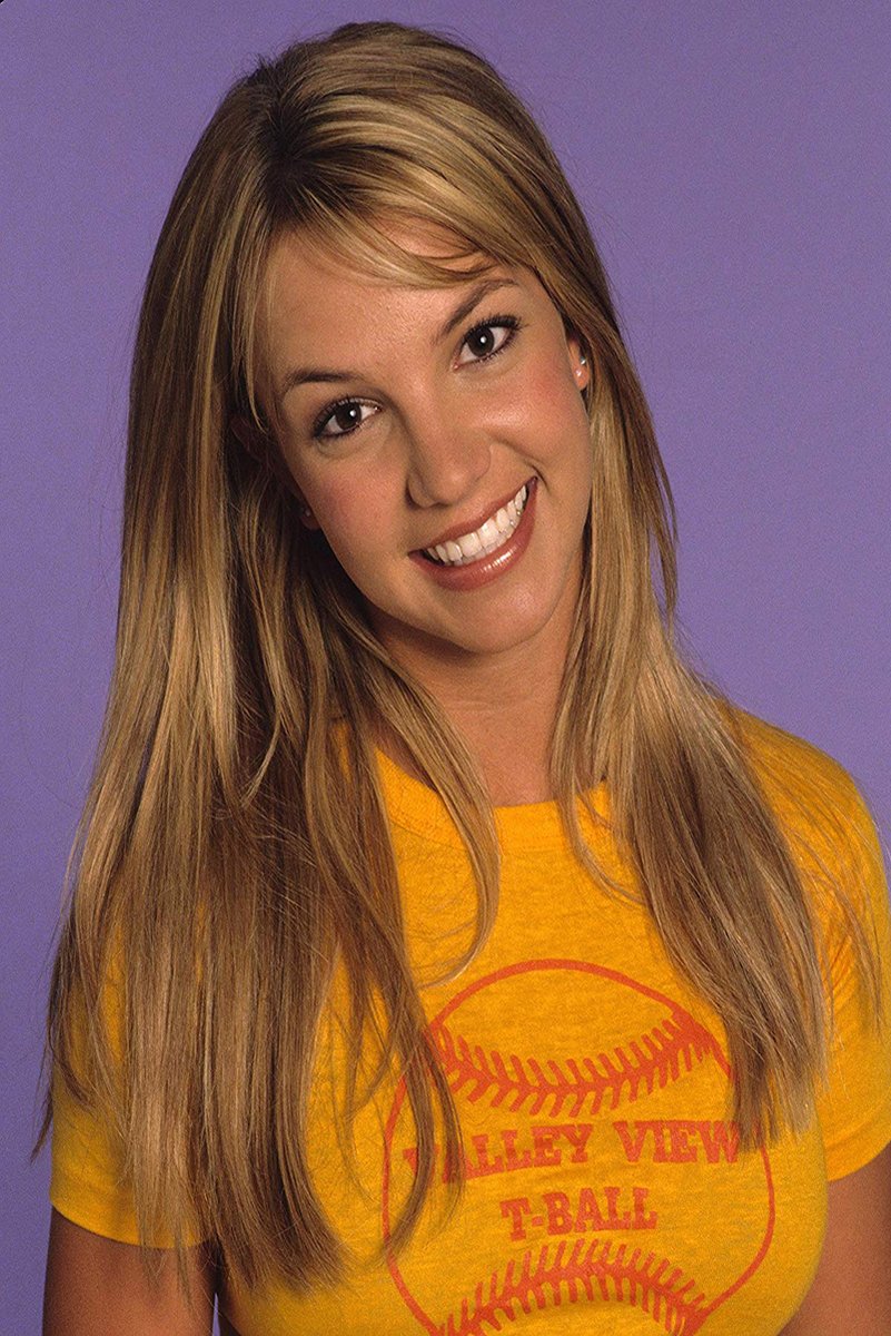 Britney Spears poster portrait with long blonde hair, smiling in a yellow T-shirt against a lavender-purple background.
