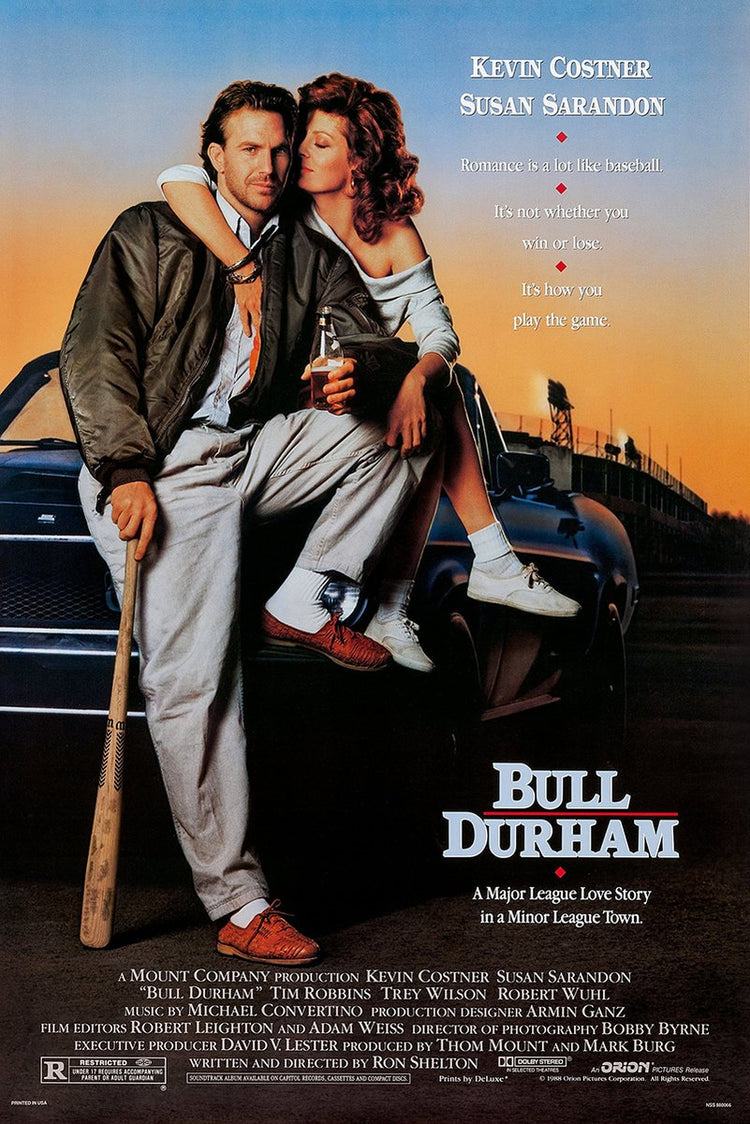 Bull Durham movie poster features Kevin Costner seated with Susan Sarandon on a car, holding a bat at sunset.