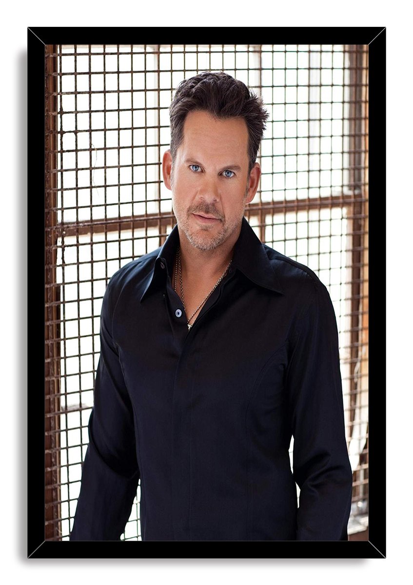 Male celebrity framed wall art print with a blue-eyed man in a black shirt before a sunlit square-grid backdrop.