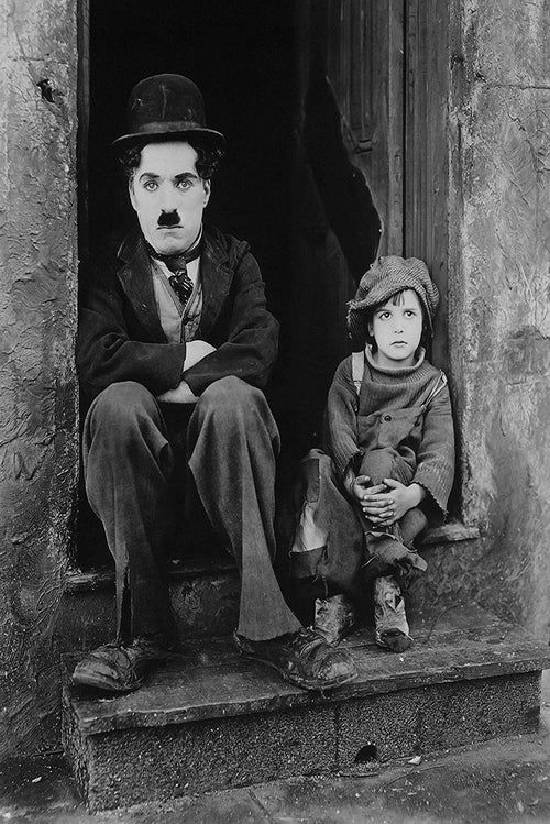 Charlie Chaplin The Kid wall art print in black and white, with Chaplin and a young boy seated in a worn doorway.