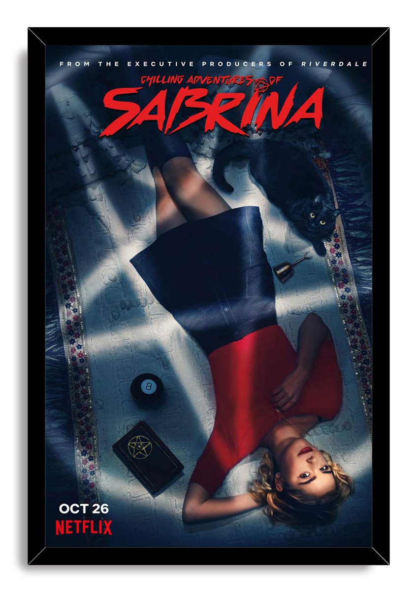 Chilling Adventures of Sabrina framed wall art print portrays Sabrina reclining in red with Salem and a pentagram-marked book.
