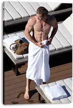 Chris Hemsworth canvas wall art print displays the shirtless actor in a white towel near loungers, folded towels, and a brown bag.