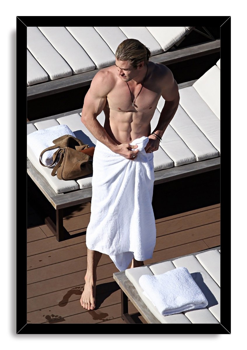 Chris Hemsworth framed wall art print portrays the shirtless actor adjusting a white towel on a wooden deck beside white lounge chairs.