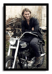Chris Hemsworth framed wall art print features the actor smiling on a black motorcycle, presented in a sleek black frame.
