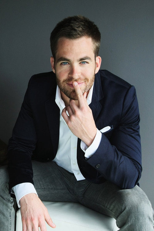 Chris Pine wall art print features the actor seated in a navy blazer and white shirt, touching his lips against a gray backdrop.