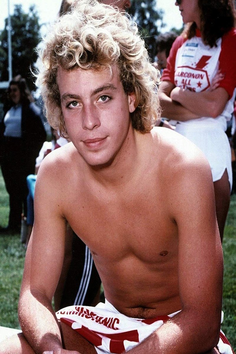Corey Haim poster features a close outdoor portrait of the curly blond actor seated shirtless with people behind him.
