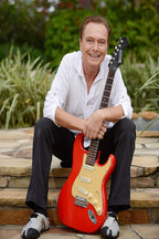 David Cassidy poster portrait of the smiling singer seated on stone steps with a red electric guitar and green garden backdrop.