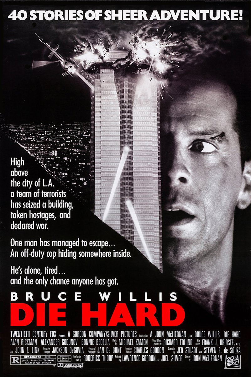 Die Hard movie poster wall art with Bruce Willis beside an exploding skyscraper, helicopter, city lights, and red title text.