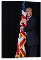 Donald Trump canvas wall art print displays him smiling as he embraces a red, white, and blue American flag on black.