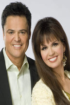 Donny and Marie Osmond poster portrait with the smiling duo in formal black, cream, and white attire against gray.