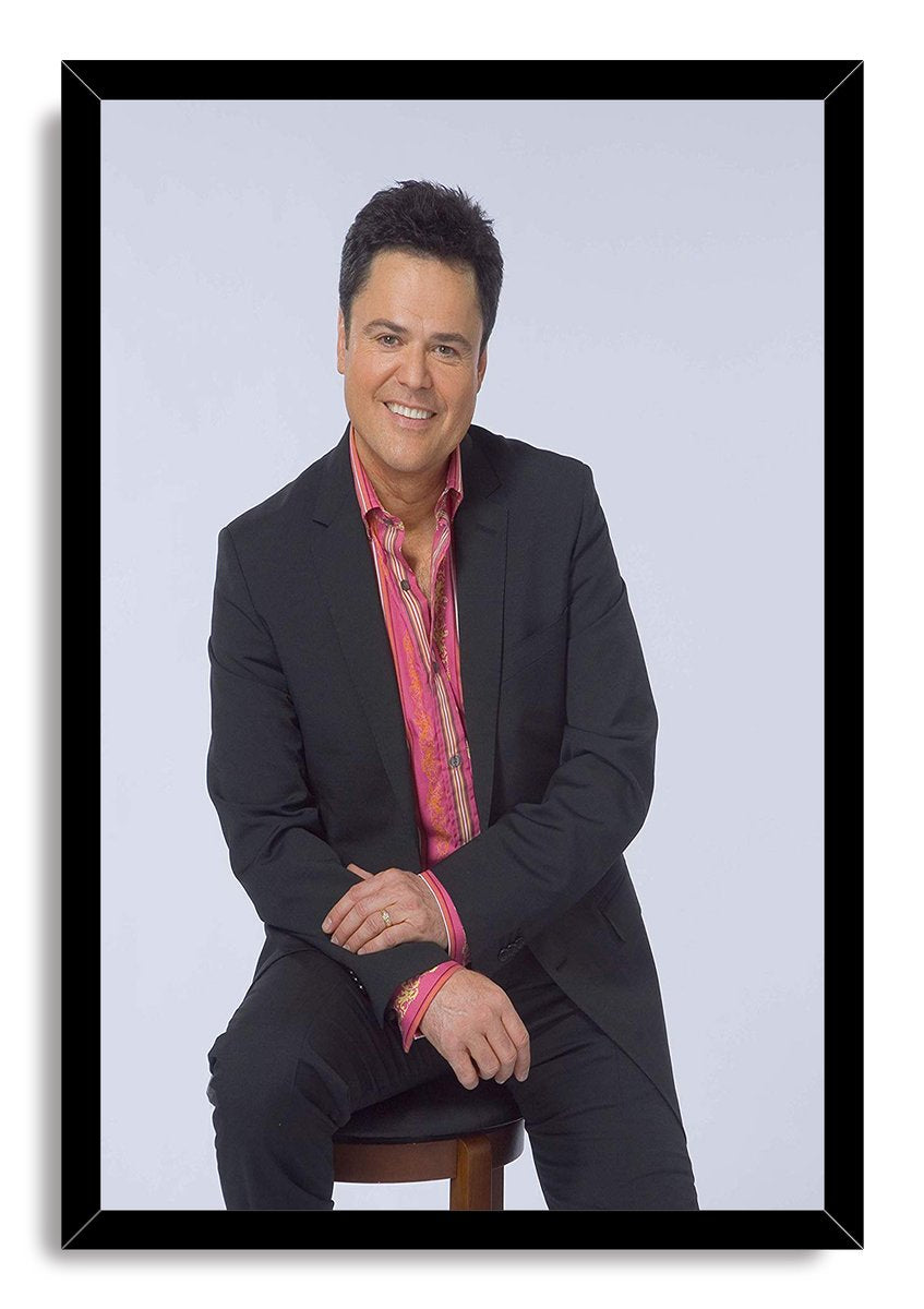Donny Osmond framed wall art print presents a smiling seated portrait in a black suit and bright pink patterned shirt.
