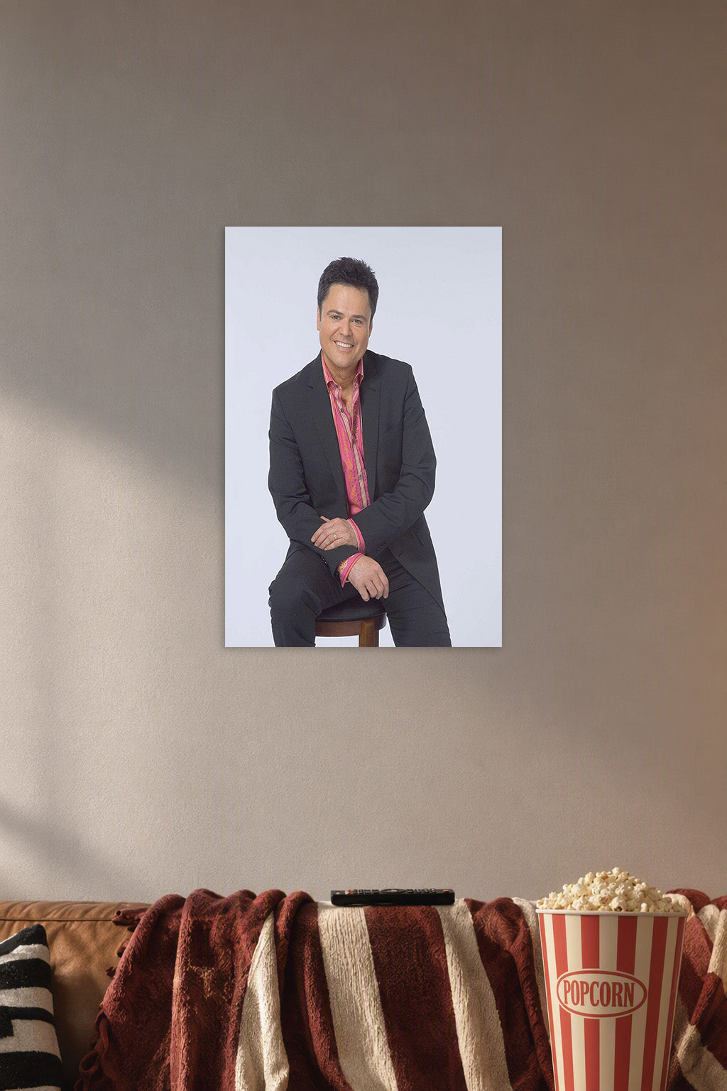 Donny Osmond in a cozy movie room above a brown sofa with popcorn.