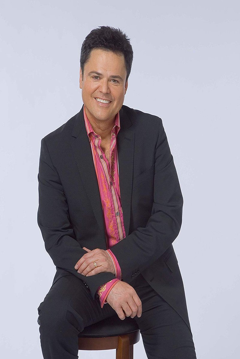 Donny Osmond poster features the smiling entertainer seated on a stool in a black suit and vivid pink patterned shirt.