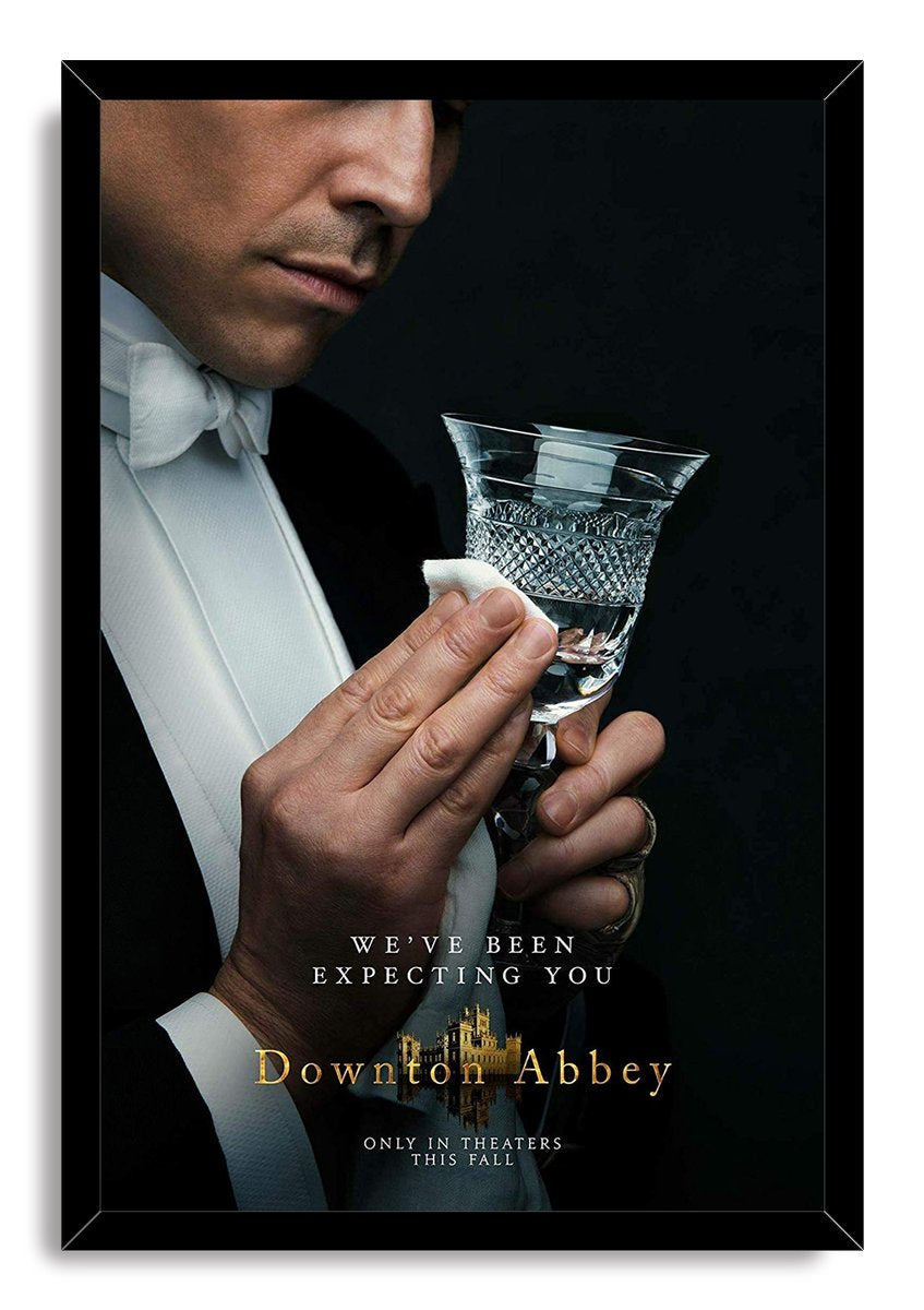 Downton Abbey framed wall art print portrays a formal butler cleaning a faceted crystal glass, set against black with white and gold lettering.
