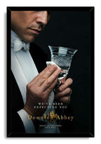Downton Abbey framed wall art print portrays a formal butler cleaning a faceted crystal glass, set against black with white and gold lettering.