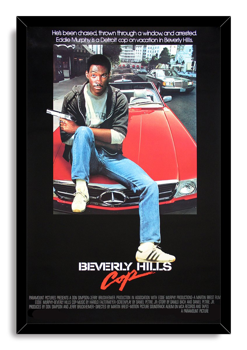 Beverly Hills Cop framed wall art print features Eddie Murphy on a red Mercedes, holding a pistol before downtown traffic.