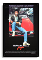 Framed Beverly Hills Cop wall art print featuring Eddie Murphy seated on a red Mercedes, holding a pistol, with bold red and white title text.