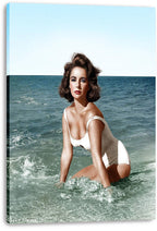 Elizabeth Taylor canvas wall art print features the actress in a white swimsuit kneeling among ocean waves, with wrapped edges visible.