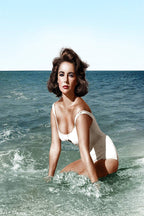 Elizabeth Taylor wall art print portrays the actress kneeling in surf in a white swimsuit beneath a pale blue sky.