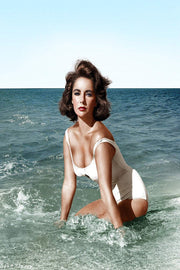 Elizabeth Taylor wall art print portrays the actress kneeling in surf in a white swimsuit beneath a pale blue sky.