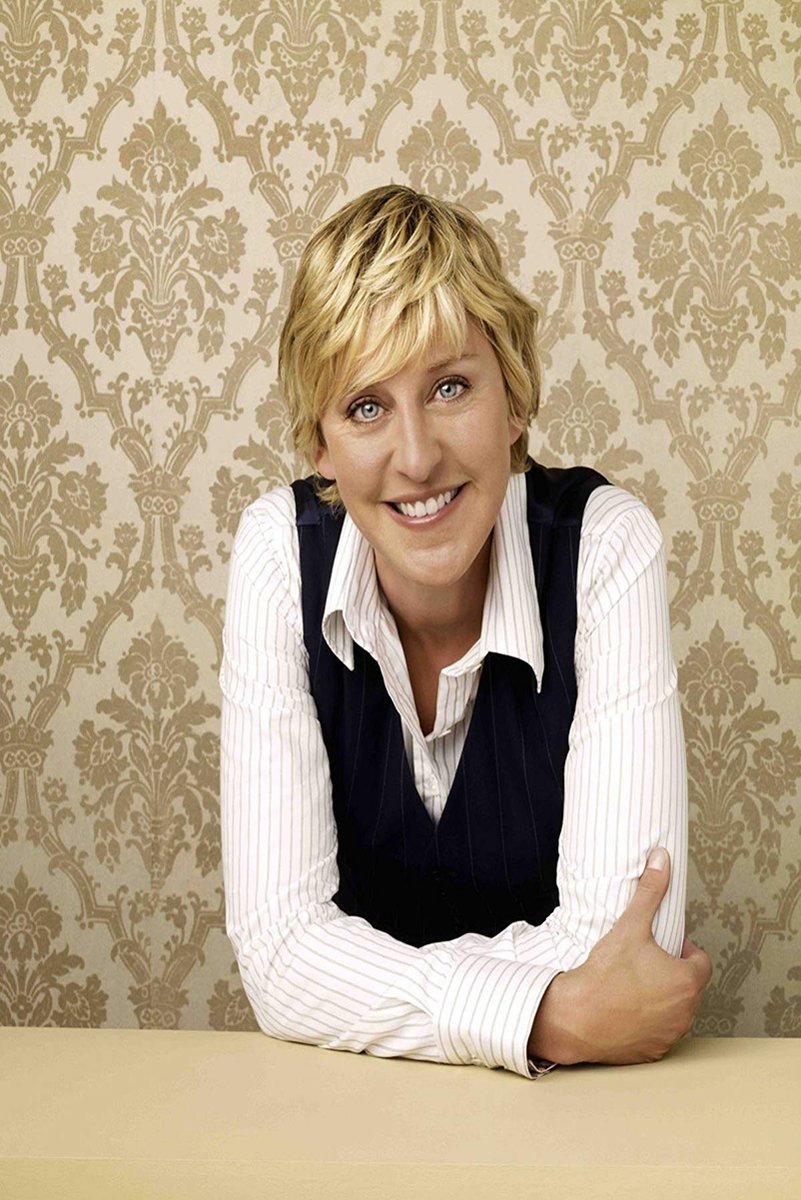 Ellen DeGeneres poster portrait of the smiling blonde host leaning forward with crossed arms before beige damask wallpaper.