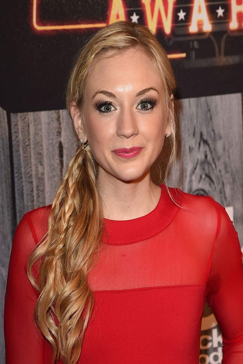 Emily Kinney poster portrait in a red sheer long-sleeve top, with braided blonde hair and neon lettering behind her.