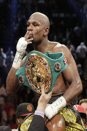 Floyd Mayweather wall art print captures the boxer kissing his fingers while wearing a green and gold championship belt in a crowded arena.