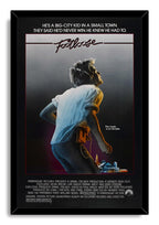 Footloose movie poster wall art print in a black frame, featuring a headphone-wearing young man and small town skyline.