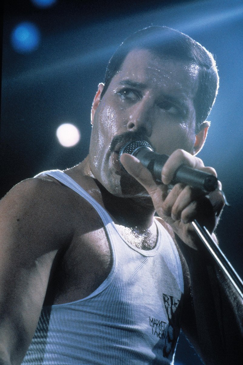 Freddie Mercury poster captures the singer in a white tank top gripping a microphone under blue stage lights.