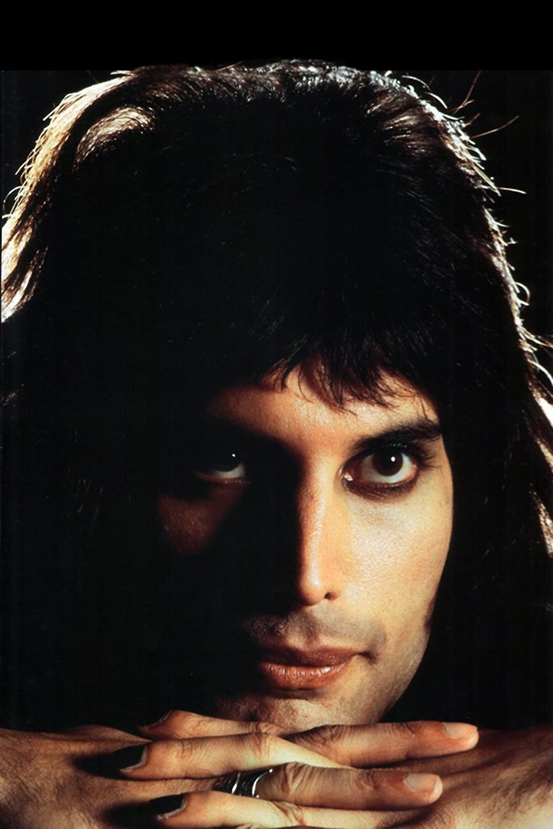 Freddie Mercury poster features a close-up, shadowed portrait with his hands folded beneath his chin against black.