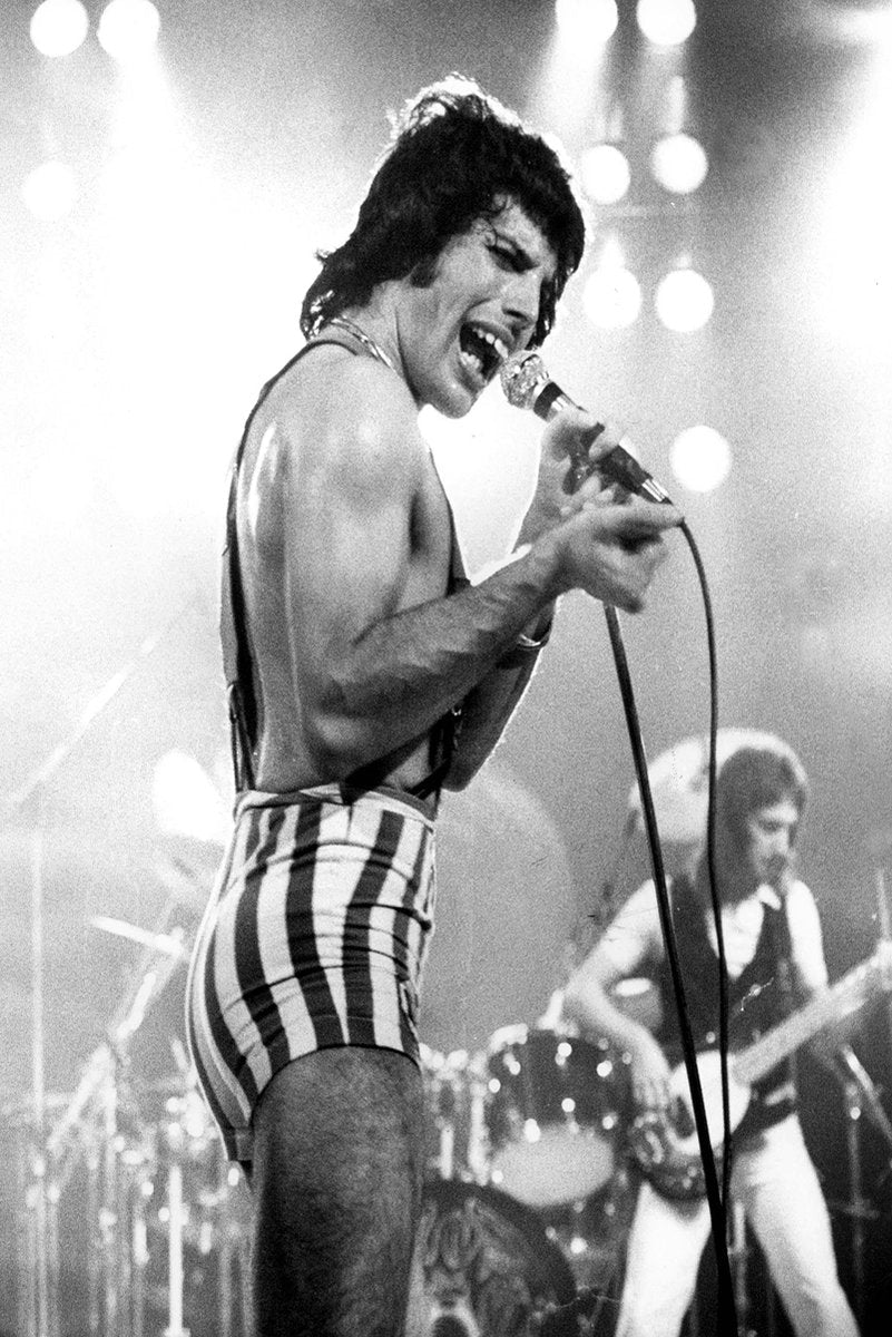 Freddie Mercury wall art print captures the singer performing with a microphone in striped shorts under bright stage lights.