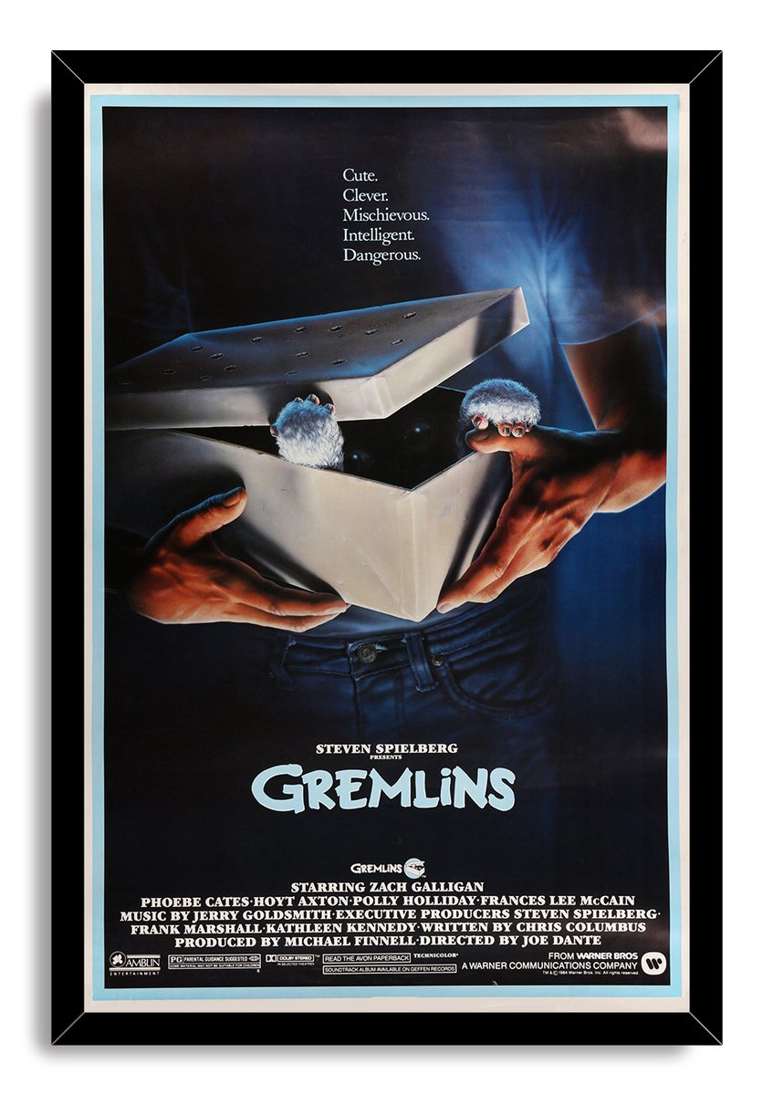 Gremlins movie poster wall art print in a black frame, with hands holding an open box and Gizmo's paws visible.