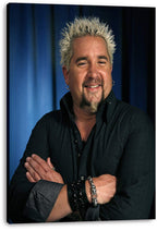 Guy Fieri canvas wall art print presents his smiling, arms-crossed portrait in a black shirt against deep blue curtains.